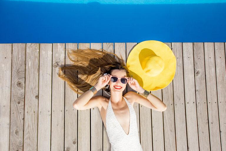 Frau am Pool. Glückliche Frau mit gelbem Sonnenhut am Beckenrand liegend.