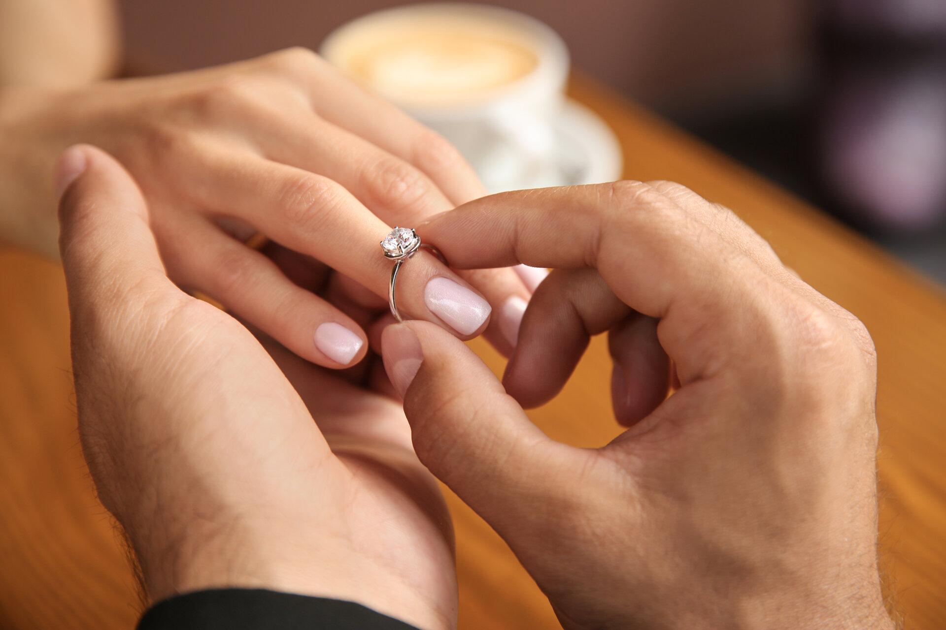 Mann steckt seiner Freundin im Café einen Verlobungsring an den Finger, Nahaufnahme