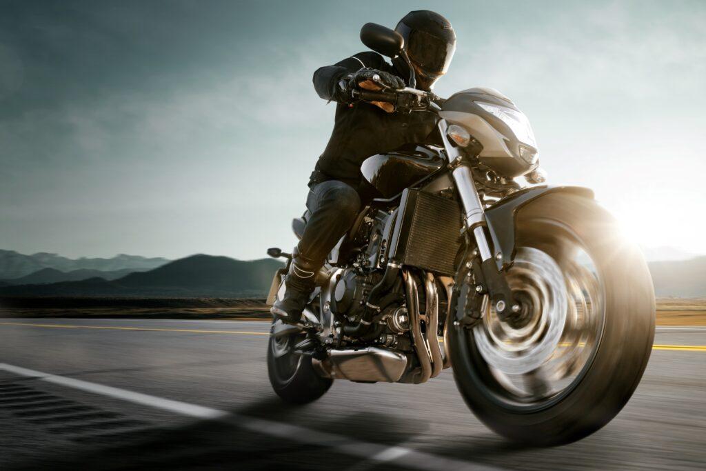 Ein Motorradfahrer in voller Fahrt auf einem 500 ccm Motorrad, eingefangen in einem Moment voller Geschwindigkeit und Freiheit, mit einer beeindruckenden Berglandschaft im Hintergrund