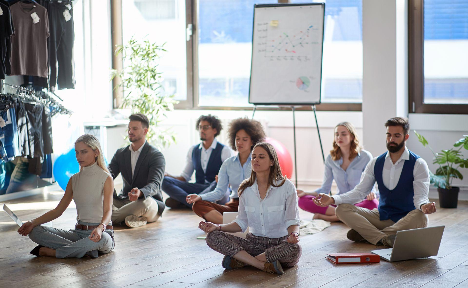 Eine Gruppe von Mitarbeitern in einem Büro, die während einer Pause Achtsamkeits- und Meditationsübungen durchführen.