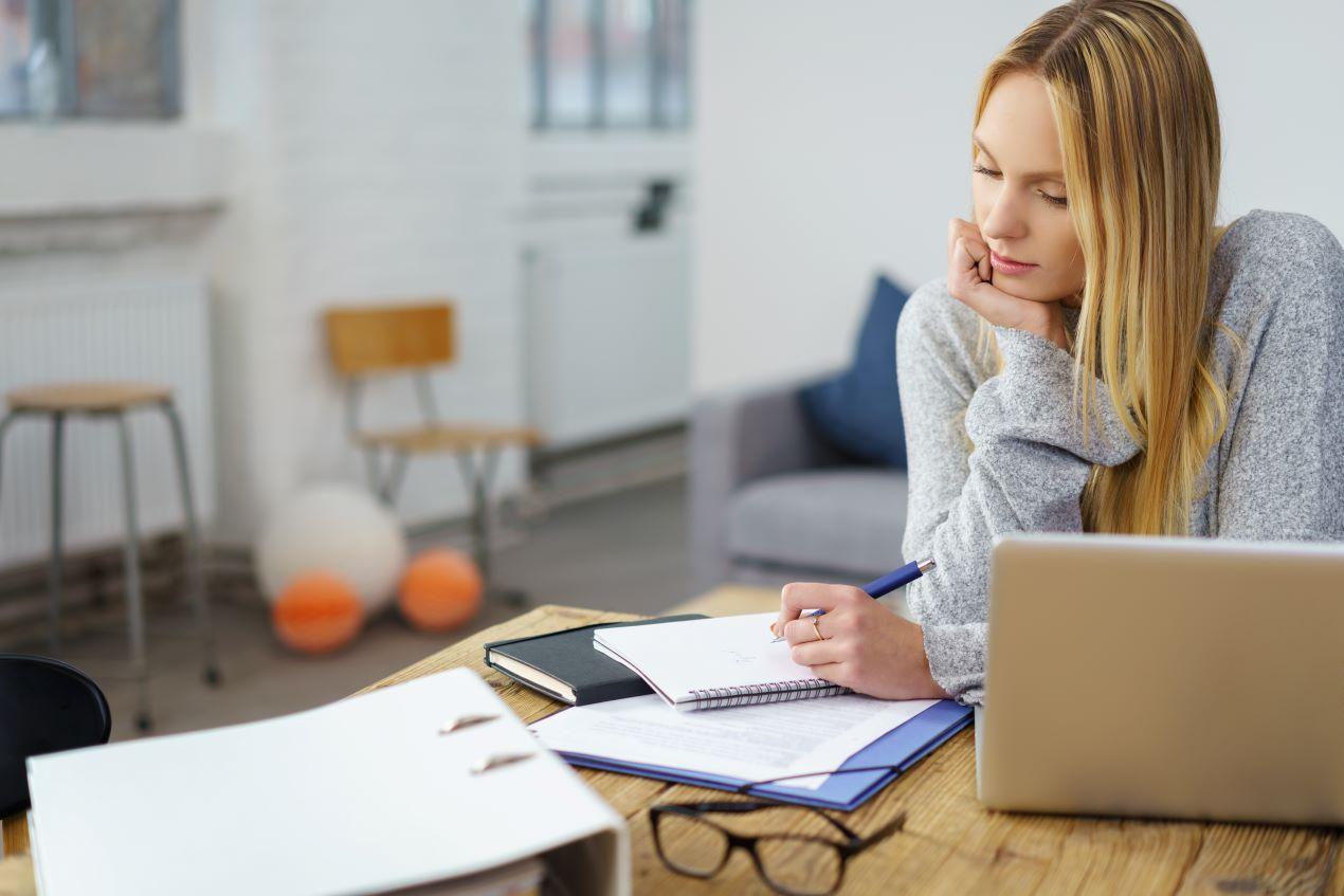 Studentin sitzt konzentriert am Schreibtisch mit Laptop und Notizen, während sie ihre Bachelorarbeit vorbereitet, möglicherweise mit der Hilfe eines Bachelor Ghostwriters.