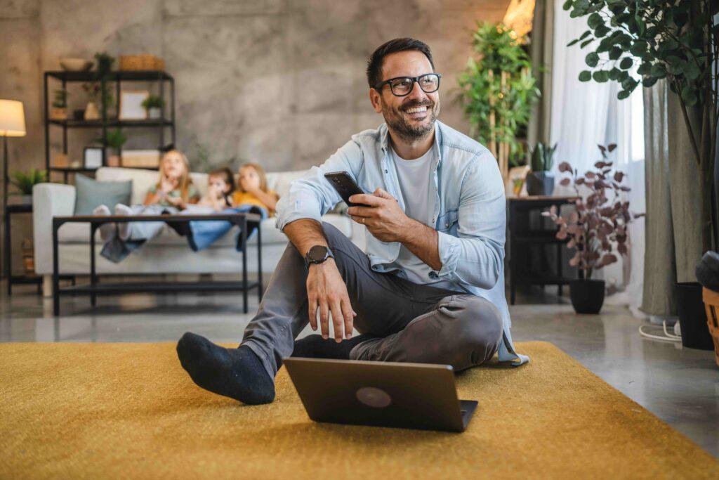 Erwachsener Mann multitaskt mit Gadgets, während die Familie entspannt auf dem Sofa sitzt.